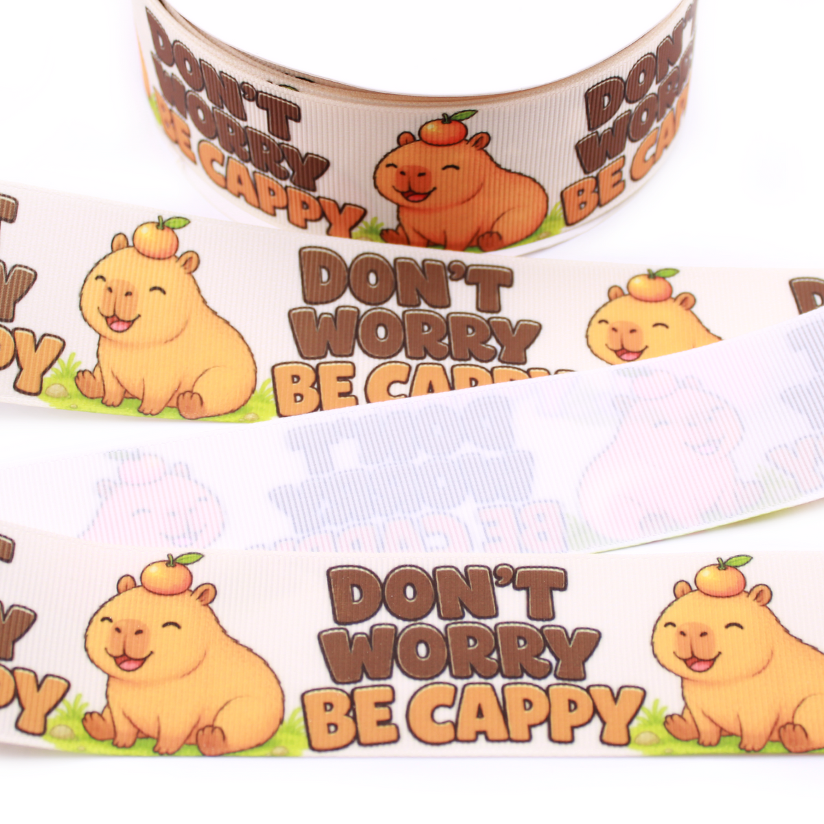 Don’t Worry Be Cappy printed grosgrain ribbon with a smiling capybara, orange on its head and brown lettering on a cream background.