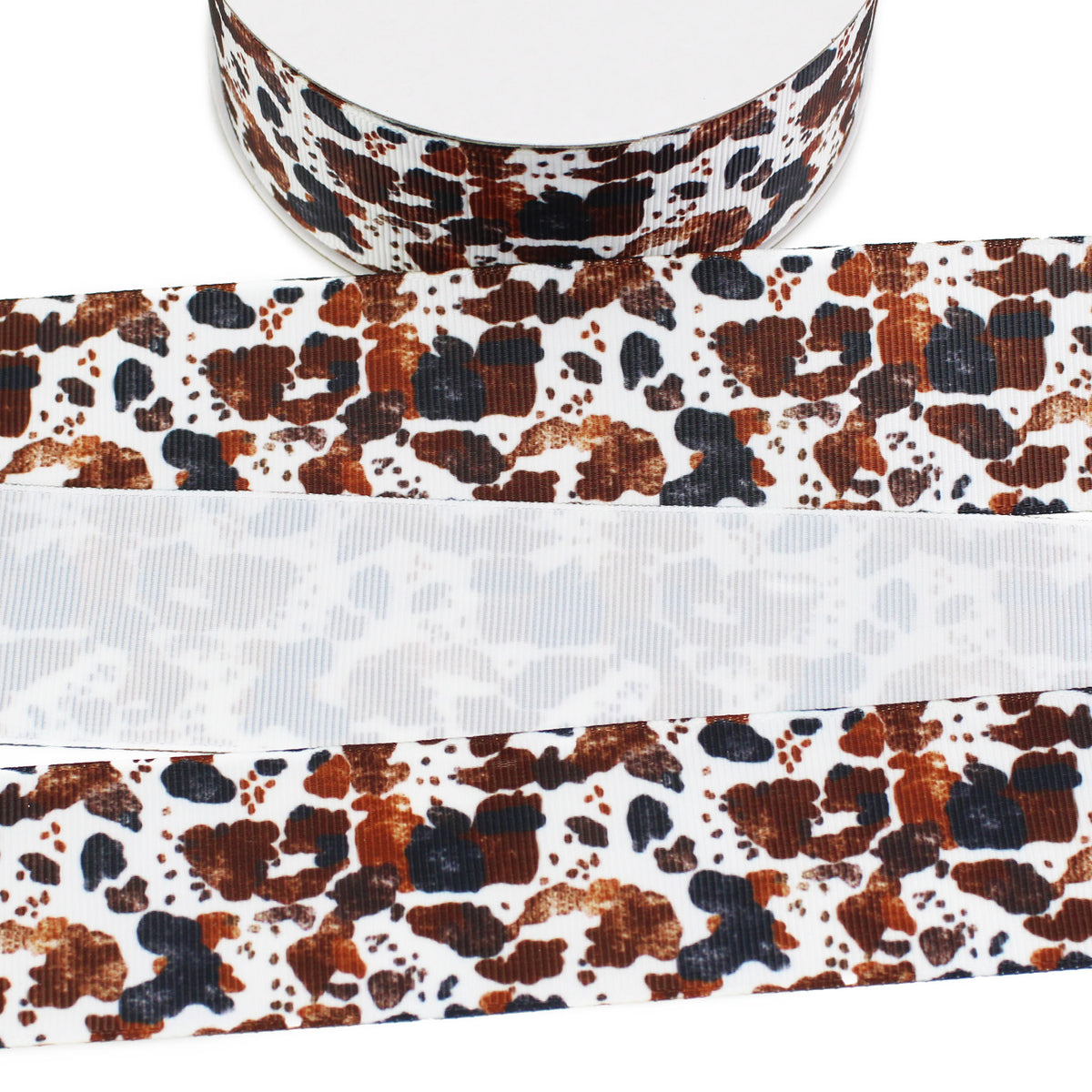 White grosgrain ribbon featuring an irregular cowhide pattern in shades of dark brown, rust, tan, and black, with the printed front and lighter reverse side visible.